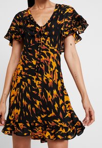 Svart klänning med orange och gula flamliknande mönster, korta fladdrande ärmar, V-ringning och dragsko-detalj vid halsringningen.