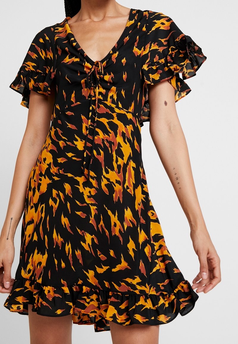 Svart klänning med orange och gula flamliknande mönster, korta fladdrande ärmar, V-ringning och dragsko-detalj vid halsringningen.