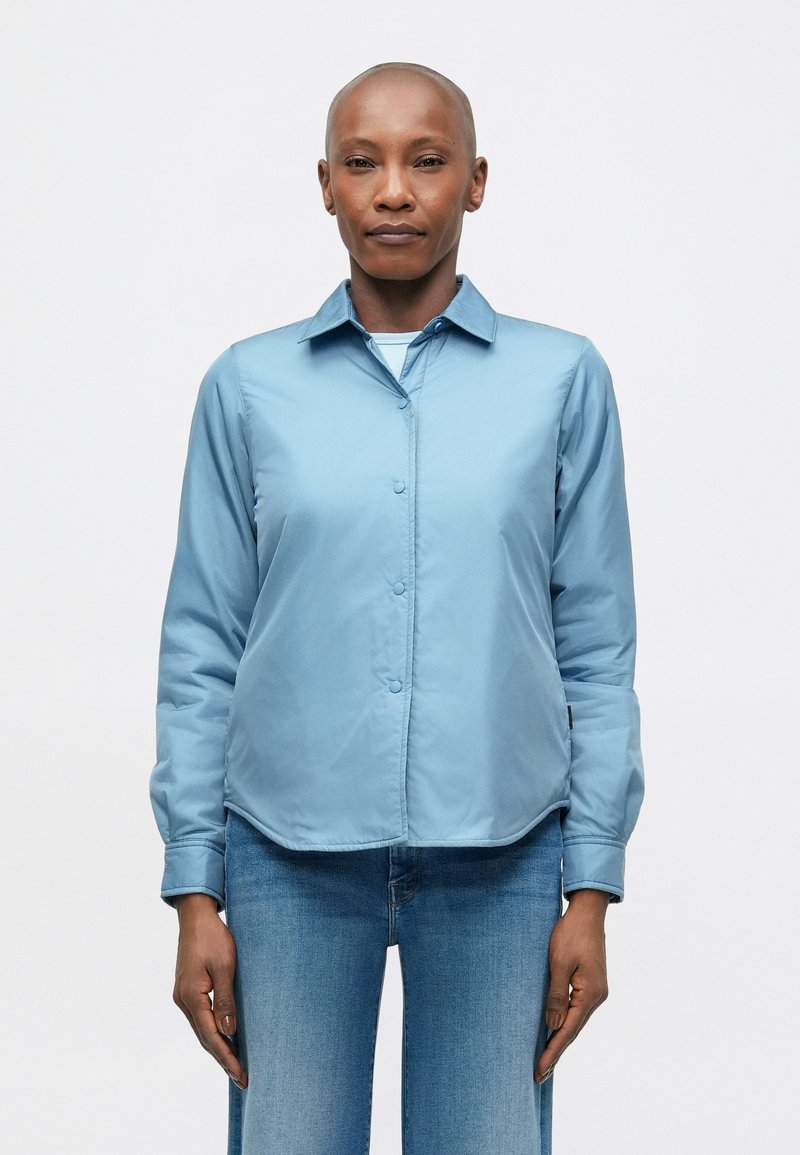  lichtblauwe overhemdd met kraag, gemaakt van een gladde stof, met lange mouwen en een afgeronde zoom. Gecombineerd met denim jeans.