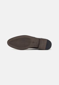 Suela de zapato de cuero marrón con una superficie lisa, ranuras horizontales para tracción y una sección del talón ligeramente elevada. Branding minimalista visible.