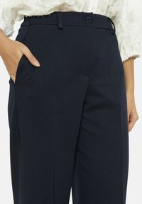 Pantalones ajustados azul marino confeccionados en tela texturizada, con cierre de botones y bolsillos laterales, con un diseño de pierna recta.