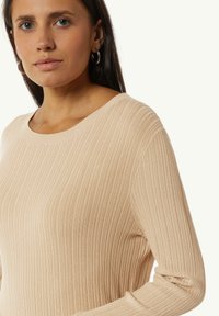 Beżowy sweter dzianinowy z prążkowanym wzorem, okrągłym dekoltem i długimi rękawami. Charakteryzuje się miękką teksturą i subtelnymi pionowymi paskami.