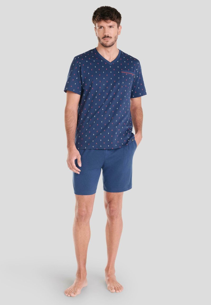 Camiseta de algodón azul marino con cuello en V, estampado pequeño de un ancla roja y bolsillo en el pecho, combinada con pantalones cortos sólidos azul marino, ambos diseñados para la comodidad y el uso casual.
