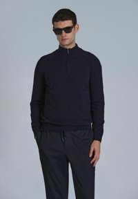 Dunkelblauer Zip-Pullover aus strukturiertem Strick, mit langen Ärmeln und tailliertem Schnitt, kombiniert mit dunklen Jogginghosen.