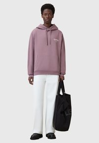 Felpa lilla con cordoncino, tasca frontale e logo bianco, abbinata a pantaloni bianchi a gamba larga e una borsa a tracolla nera. Tessuto dalla consistenza liscia.