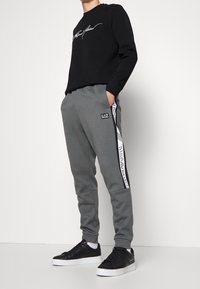 Svart sweatshirt med vit signaturtryck, ihopparad med grå mjukisbyxor som har logotryck längs sidan. Svarta sneakers fulländar outfiten.