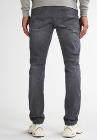 Vaqueros de mezclilla gris con un corte ajustado, un leve desvanecimiento, dos bolsillos traseros y una cintura de altura media. Combinados con zapatillas de color claro.