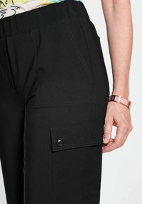 Zwarte cargo-broeken met elastische taille, voorzien van zijzakken, met contrasterende stiksels en knoopaccenten. Het materiaal lijkt soepel en duurzaam te zijn.