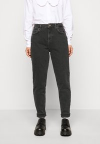 Svarta denimjeans med slim fit, femficksdesign och uppvikta benslut, kombinerat med svarta snörskor och en vit skjorta med krage.