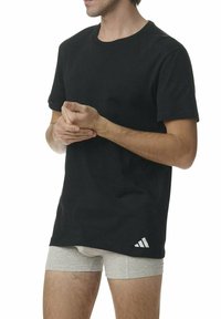 T-shirt en coton noir avec un col rond et des manches courtes. Présente un accent logo sur le bas à gauche. Associé à un short de sport gris.