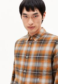 Ruitjesoverhemd in oranje, grijs en wit. Voorzien van een knoopsluiting, kraag en een enkele borstzak met een klein logo.