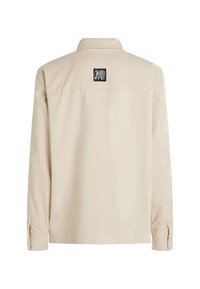 Beige corduroy overhemdjack met een kraag, lange mouwen en een rechthoekig zwart etiket op de bovenrug. Gestructureerd oppervlak.
