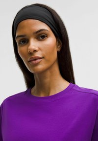 Violeta kokvilnas T-krekls ar noapaļotu kakla izgriezumu, ar gludu tekstūru. Melna auduma galvas lente, kas uzlikta uz taisniem tumšiem matiem.