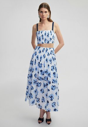 Set di abbigliamento composto da due pezzi, caratterizzato da un top corto con spalline blu e una lunga gonna realizzata in tessuto bianco decorato con motivi floreali blu.