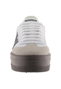 Sneakers bianchi con punta in suede beige, accenti neri ai lati e suole in gomma grigia testurizzata. Presentano un design di allacciatura bianca prominente.