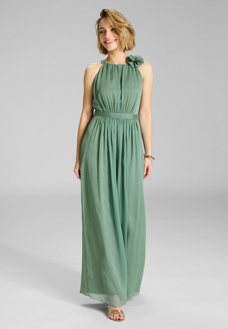 Maxikleid aus weichem grünem Stoff; Neckholder-Ausschnitt mit floralem Akzent an einer Schulter; fließende Silhouette mit gerafftem Taillenbereich.