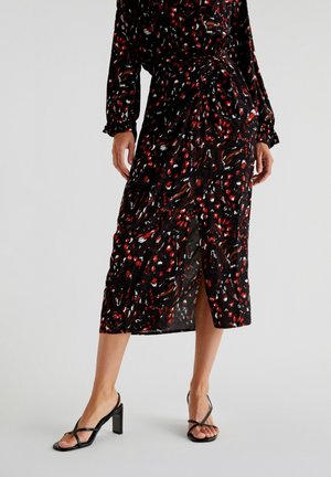 Rochie midi neagră cu un model vibrant de accente roșii și albe, material texturat și o fante laterală, purtată cu sandale negre cu bretele.