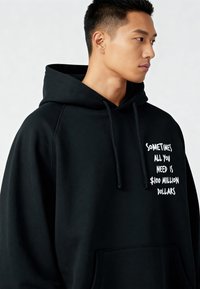 Felpa nera con cappuccio e ampia tasca frontale, con testo bianco che recita: "A volte tutto ciò di cui hai bisogno sono 100 milioni di dollari."