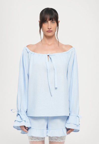 Blouse bleu clair à épaules nues avec de longues manches fluides, fermeture à nouer au niveau du col et accents à volants aux poignets, assortie avec des shorts de la même couleur.