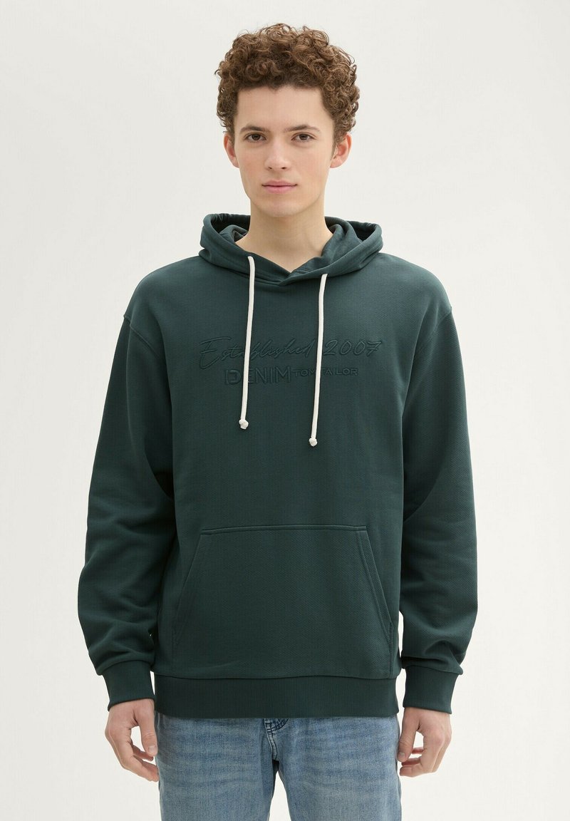 Ciemnozielona bluza z kapturem w teksturowym materiale, z kieszenią typu kangurka, sznurkiem przy kapturze oraz haftowanym detalem "Established 2007" z przodu.