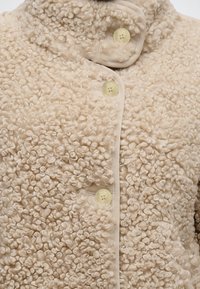 Veste en polaire beige bouclée avec un col montant et trois boutons couleur crème sur le devant.