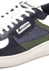 Zapatilla de cuero con cuerpo principal en azul marino, acentos de gamuza verde y detalles en blanco. Presenta un panel lateral con un patrón geométrico y cordones blancos.