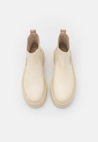 Bottines beiges en cuir lisse avec des panneaux latéraux élastiques, une semelle en caoutchouc texturée et une languette à l'arrière pour un enfilage facile.