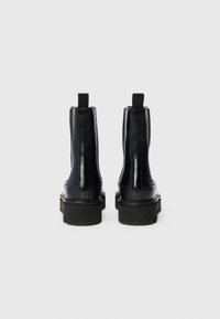 Bottines en cuir noir avec une finition brillante, panneaux latéraux élastiques et semelles en caoutchouc robustes. Comprend des languettes de traction pour un enfilage facile.