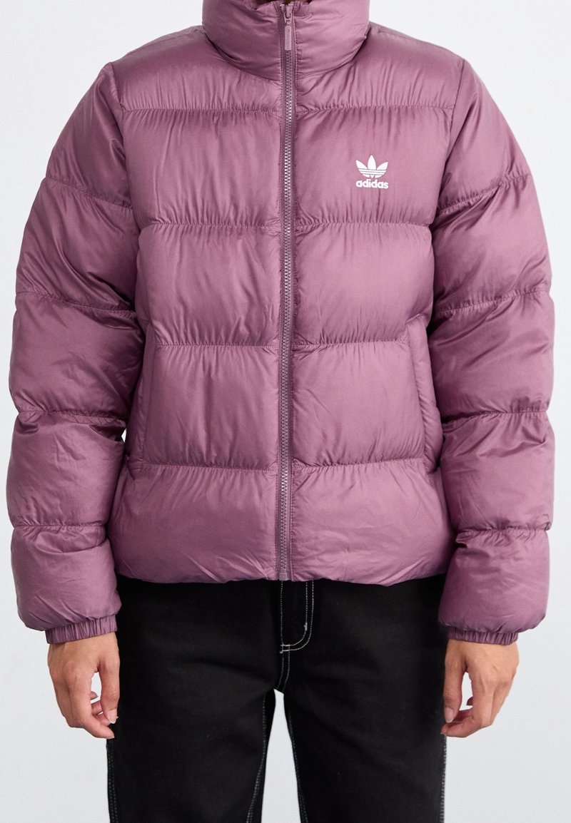 Lila puffjacka med hög krage, dragkedja fram och vit adidas-logga på vänster bröst. Har kviltat mönster och elastiska ärmslut.