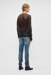 Camisola de malha canelada castanho escuro com mangas compridas, combinada com jeans azuis desbotados e botas pretas de salto, vista por trás.