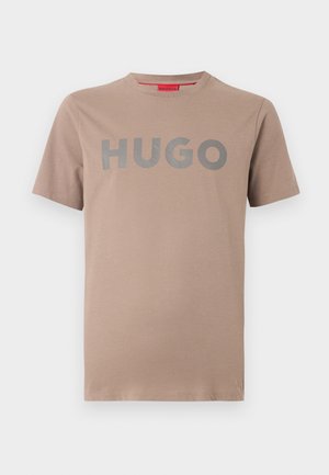 Beige kortærmet t-shirt med rund hals og stor grå "HUGO" tekst trykt på brystet, ensfarvet baggrund.