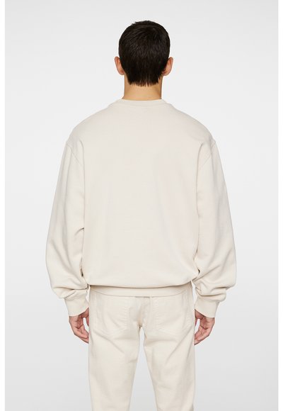 Beige sweatshirt med nedsunkne skuldre, blød tekstur og en løs pasform, parret med matchende beige bukser. Bagfra, ingen synlige grafik.