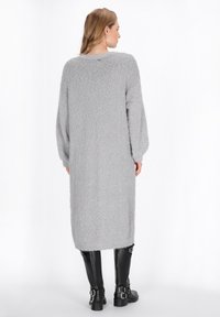 Langes graues Strickkleid mit flauschiger Textur, runder Halslinie und Ballonärmeln, kombiniert mit schwarzen Lederstiefeln mit Schnallen.