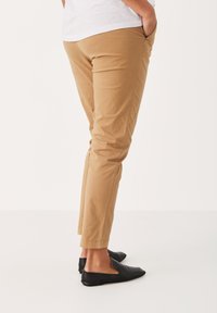 Tan chinos with a tailored fit, featuring side pockets and a smooth, lightweight fabric. Worn with black slip-on shoes.