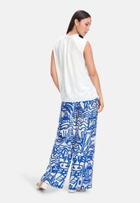 White sleeveless top with a gathered back, paired with wide-leg blue pants featuring a white abstract pattern and light fabric texture.