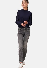 Pull marin avec des manches longues plissées, associé à un jean gris et des baskets blanches. Tissu doux avec des accents côtelés sur les manches.