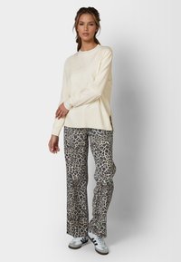 Cream long-sleeved sweatshirt with embossed logo, paired with flared leopard print pants. White sneakers with black stripes complete the look.