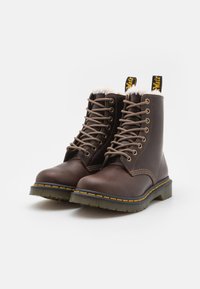 Bottines en cuir marron à lacets, avec un intérieur en peluche, des coutures jaunes et une semelle en caoutchouc épaisse avec un motif de tread texturé.