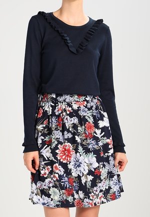 Navy long-sleeve top with ruffled neckline paired with a floral-patterned skirt featuring red, blue, and green flowers on a dark background.