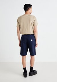 Beige cotton T-shirt and navy shorts with patch pockets. Model wears black shoes with a textured finish and short black socks.