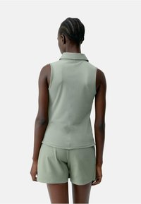 Groene mouwloze polo en bijpassende shorts van zacht materiaal, met een kraag en een eenvoudig ontwerp, gezien vanaf de achterkant.