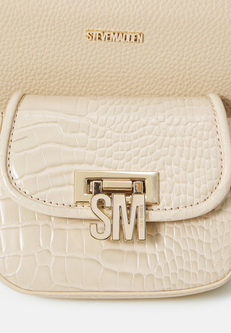 Beige Handtasche mit Krokodilprägung und glatter Textur, ausgestattet mit einem goldfarbenen Metallverschluss, der "SM" zeigt, und einem dezenten Logo, das darüber eingeprägt ist.