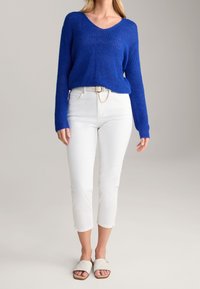 Niebieski dziergany sweter, białe spodnie typu cropped z paskiem ozdobionym łańcuszkiem oraz jasne klapki, tworzące casualowy strój.