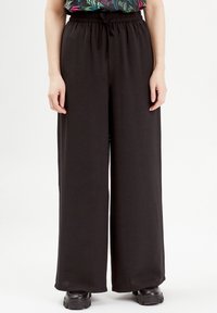 Pantalon noir à jambes larges en tissu lisse et extensible, doté d'une taille élastique avec cordon de serrage et d'une coupe décontractée.