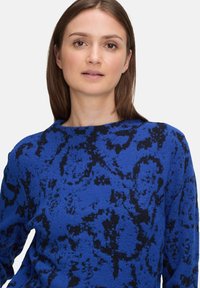 Sweter w kolorze intensywnego niebieskiego o teksturowanym, puszystym wykończeniu. Posiada czarne abstrakcyjne wzory oraz klasyczny okrągły dekolt.