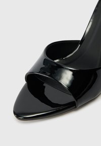 Fekete lakkbőr, magas sarkú cipő hegyes orral és keresztpántos kialakítással. Simább textúra és fényes felület. Nincs látható fémalkatrész.