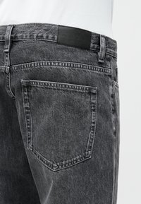 Mustad tumesinised teksad, millel on pleekinud disain, sirge sääre lõige, tagatasku ja nahast brändipatch vööl.