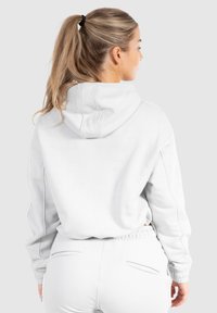 Hellgrauer Kapuzenpullover mit Kordelzug, gerippten Bündchen und Kängurutasche. Weicher Stoff mit lockerer Passform, kombiniert mit passenden Hosen.