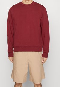 Felpa bordeaux con maniche lunghe, collo e polsini a costine, abbinata a pantaloni corti beige. Tessuto morbido con una vestibilità comoda.