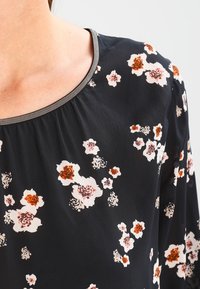 Blouse noire à motifs floraux avec des fleurs roses et oranges éparpillées, un col rond avec une bordure texturée, et un tissu doux et léger.